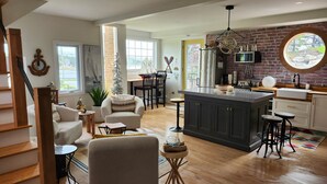A spacious living area with a kitchen, wooden flooring, and a large window providing natural light.