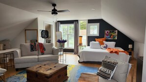 A modern loft bedroom with a large bed, a sofa, a wooden chest, and a ceiling fan.