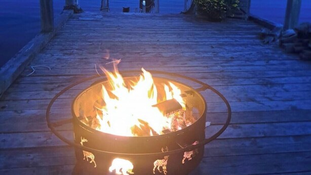 A wooden dock with a fire pit in the center, overlooking a calm body of water at dusk.
