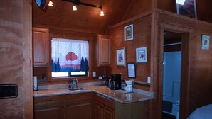 A compact kitchen with wooden cabinets, a window with a view of mountains, and a coffee maker. - The Shack #4                . (Williams)