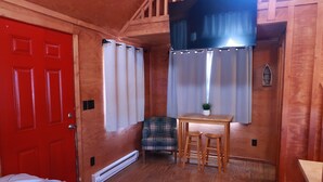 A room with a red door, a plaid chair, a small table with stools, and a window with curtains. - The Shack #4                . (Williams)
