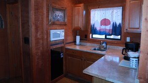 A kitchen with wooden cabinets, a microwave, a coffee maker, and a window with a view of trees. - The Shack #4                . (Williams)