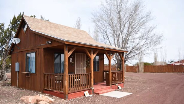 A wooden cabin with a porch, satellite dish, and a fenced yard. - The Shack #4                . (Williams)