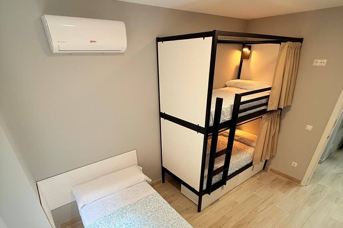 Une petite pièce comprenant un lit simple, un lit superposé et un climatiseur fixé au plafond.