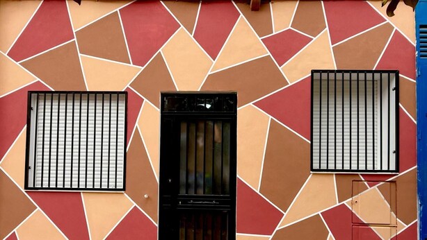 Fachada de prédio com padrão geométrico em azulejos vermelhos, laranjas e bege.