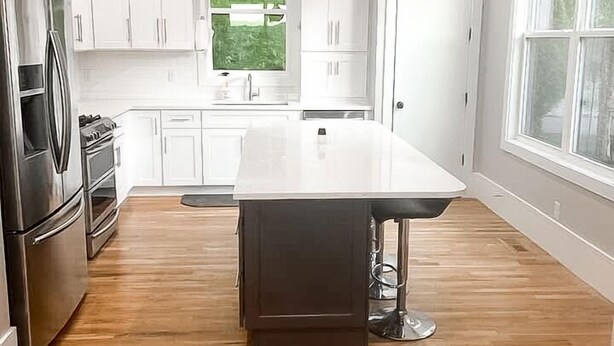 A modern kitchen with white cabinets, a central island, stainless steel appliances, and a large window providing natural light.