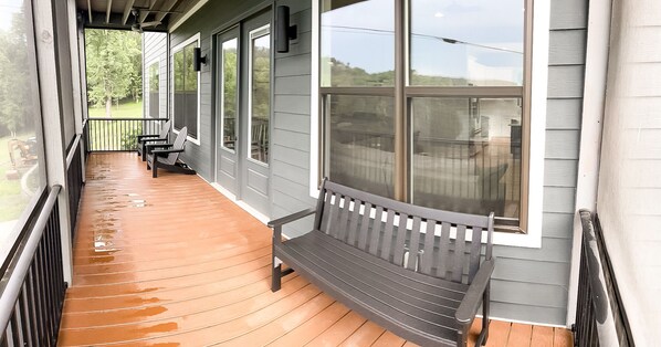 A wooden porch with a bench and a view of a green landscape.