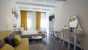 A modern hotel room with a bed, a sofa, a desk, and a TV.