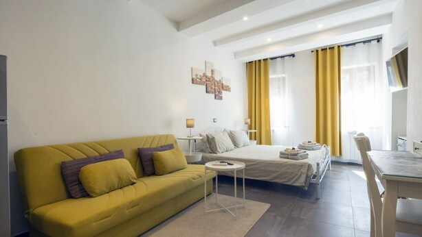 A modern hotel room with a yellow sofa, a bed, a small table, and a desk.