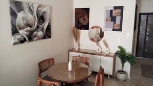 Un coin repas avec une table ronde en bois, deux chaises en bois, un vase blanc et une plante en pot.