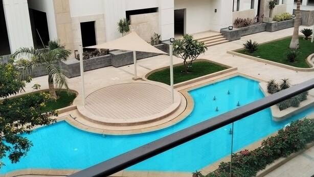 Un bâtiment moderne doté d’une piscine, entouré de verdure et agrémenté d’une terrasse couverte.