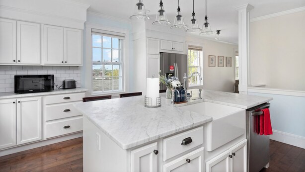 A modern kitchen with white cabinetry, a marble countertop, and a stainless steel refrigerator.