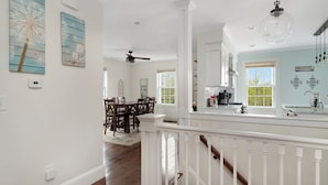 A spacious kitchen with white cabinetry, a dining area with wooden chairs, and a staircase with white railings.