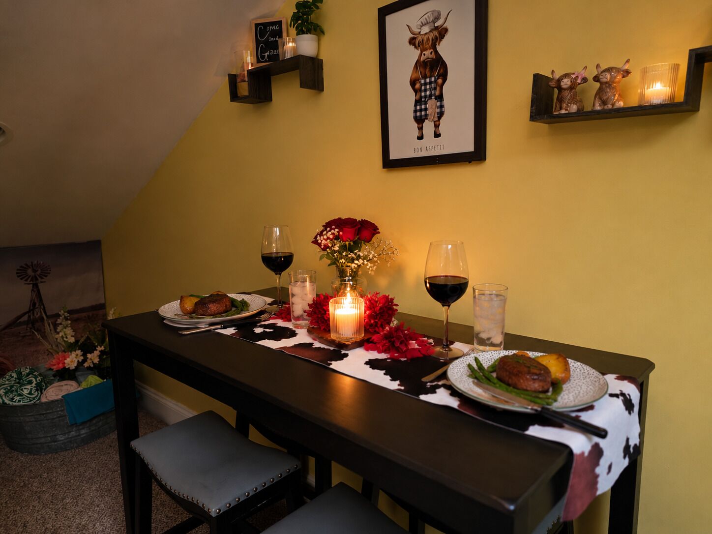 Una mesa de comedor dispuesta con platos, vasos y velas, con un cuadro enmarcado y elementos decorativos en la pared.