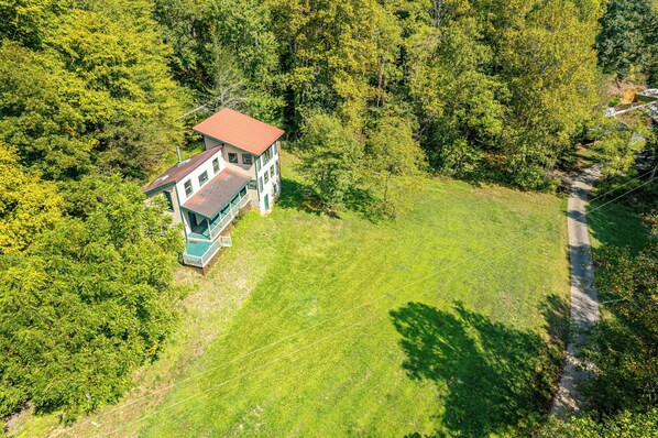Vista aérea de una casa rodeada de un bosque denso, con un camino despejado que lleva a la entrada.