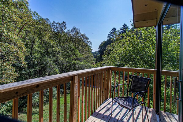En træterrasse med en metalstol, omgivet af tæt, grøn beplantning.