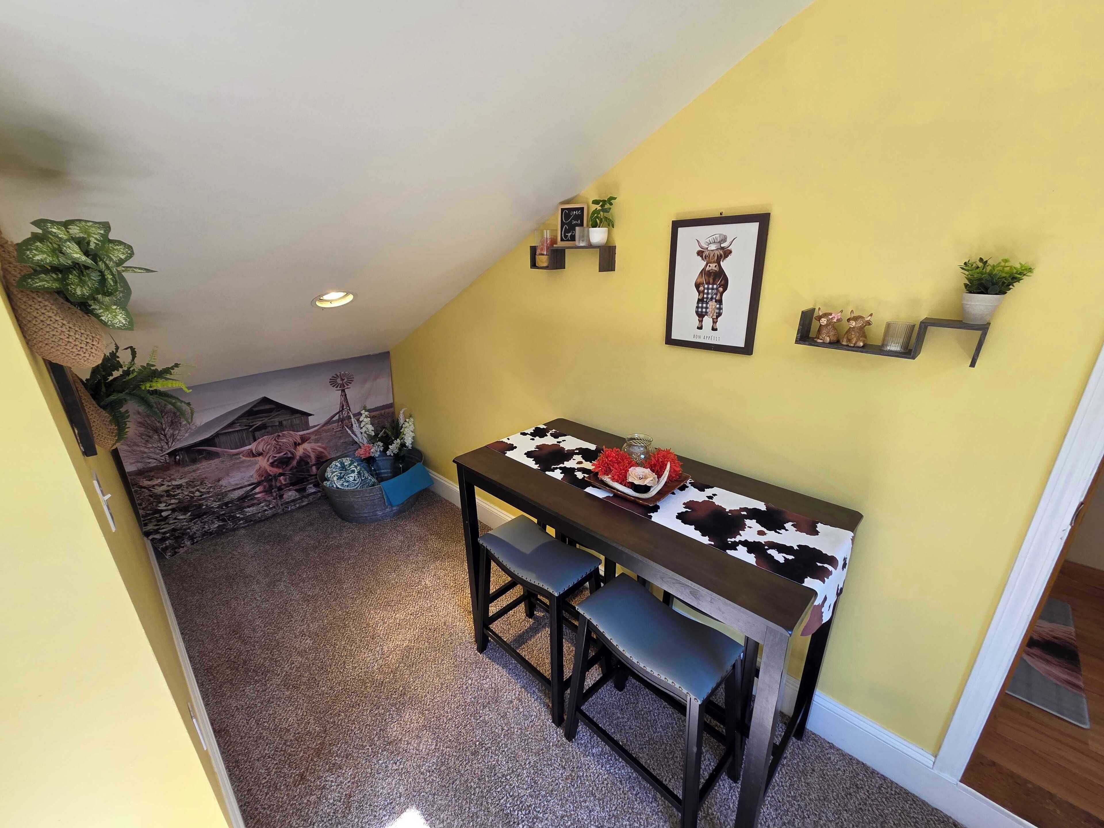 A dining area with a table and chairs, a wall-mounted shelf with decorative items, and a framed picture.