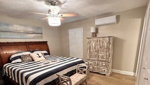 A bedroom with a wooden bed, a nightstand, a wooden chair, a ceiling fan, and a wall-mounted air conditioner.