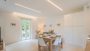 A modern dining area with a wooden table, white chairs, and a glass-top table. There are framed pictures on the walls and a door leading to a balcony. - Magnolia House Como by Rent All Como (Como)
