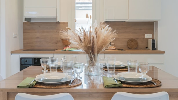 A modern kitchen with a wooden countertop, a dining table set with clear glassware and plates, and a decorative vase with pampas grass. - Magnolia House Como by Rent All Como (Como)