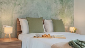 A neatly made bed with pillows, a bedside table with a lamp, a tray with croissants and cups, and a book on the bed. - Magnolia House Como by Rent All Como (Como)
