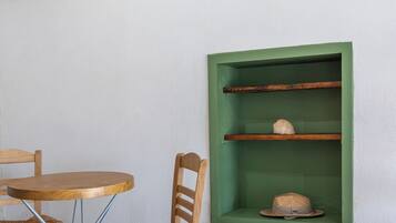 Una habitación con una mesa redonda de madera y dos sillas de mimbre, un estante verde con un sombrero, y un letrero de madera en la pared.