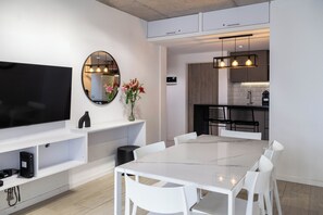 Una cocina moderna con armarios blancos, una encimera de mármol y un comedor con mesa y sillas blancas.
