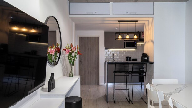 A modern kitchen with white cabinetry, a black countertop, a large mirror, and a vase with flowers. - BT Homes - Palermo, Oro  (Buenos Aires)