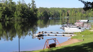 A lakeside dock with boats, a swing set, and a grassy area. - Lakeview+Sunny Beach+RELAXING 3 BR Home on Lake Thompson with WiFi, Central AC (Rhinelander)