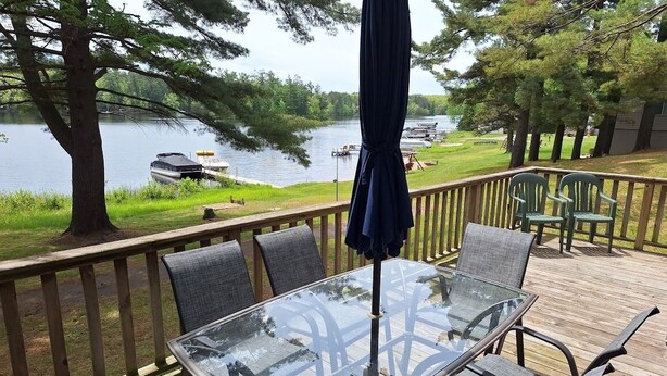 A glass-top table with six chairs on a wooden deck overlooking a lake with boats. - Lakeview+Sunny Beach+RELAXING 3 BR Home on Lake Thompson with WiFi, Central AC (Rhinelander)