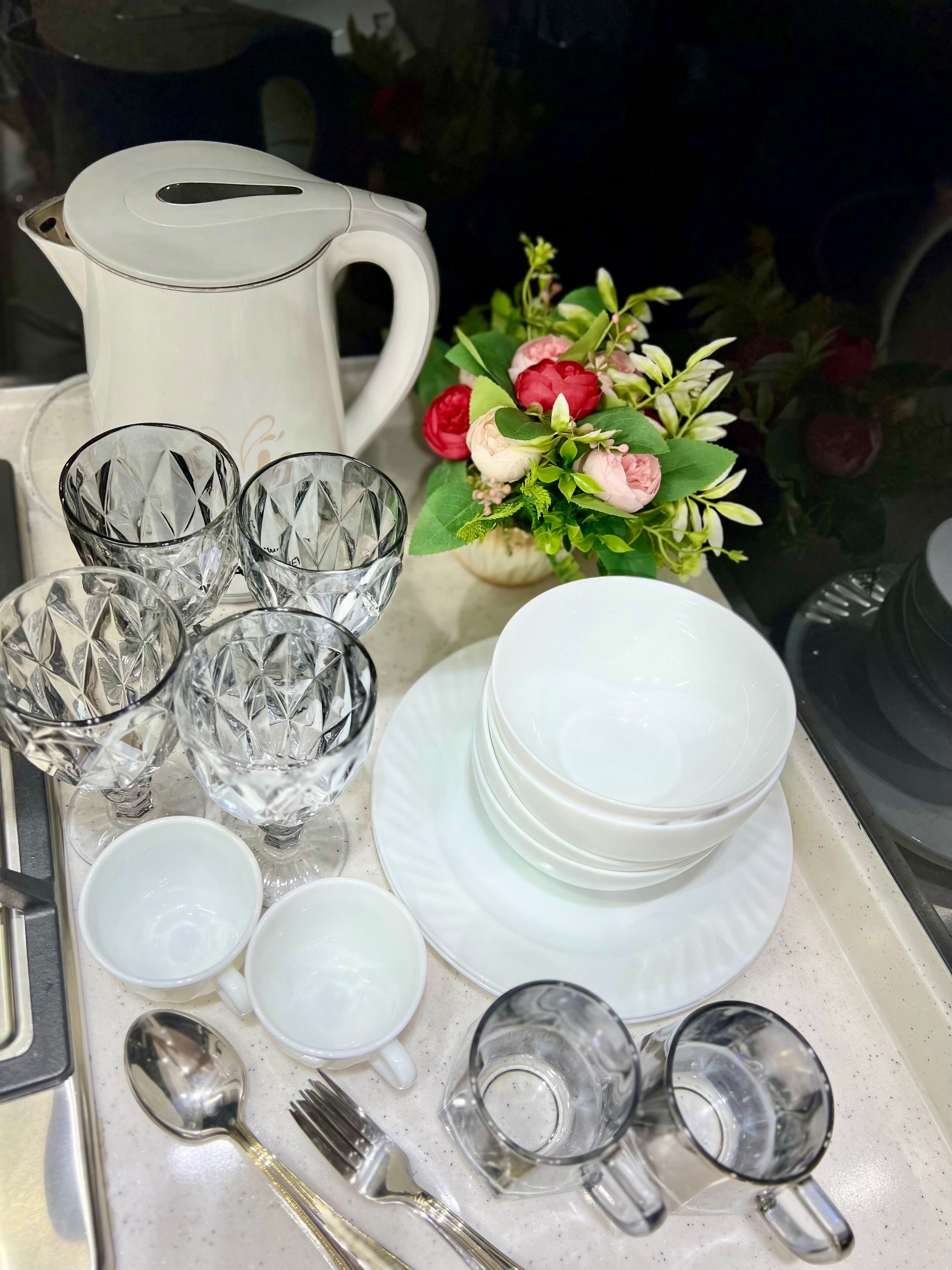 A tray with various glassware, including multiple glasses, a pitcher, and a floral arrangement.