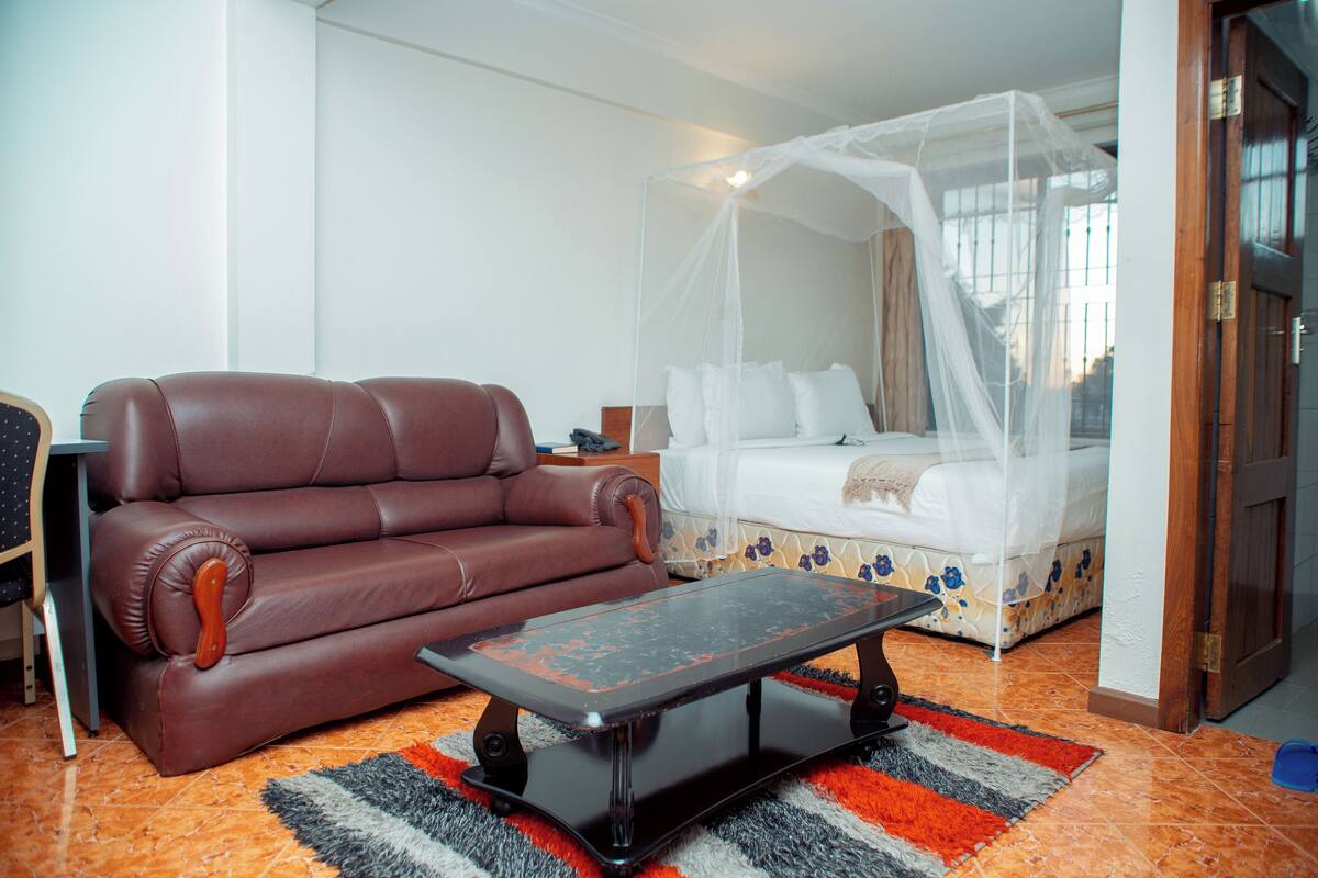 A room with a brown leather sofa, a bed with a white canopy, and a black coffee table.