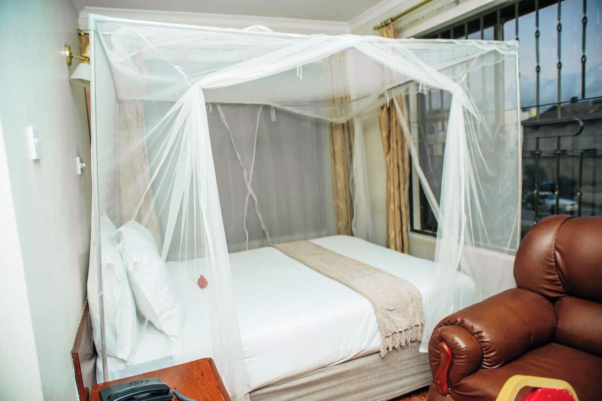 A single bed with a mosquito net, a leather armchair, and a bedside table with a telephone.
