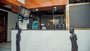 Un espace d’accueil doté d’un plafond en bois, d’un téléviseur fixé au mur et de deux statues placées de part et d’autre du comptoir d’accueil.