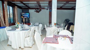 Une salle de banquet avec des tables rondes recouvertes de nappes blanches, chacune agrémentée d’un set de table à carreaux et d’un petit vase de fleurs.