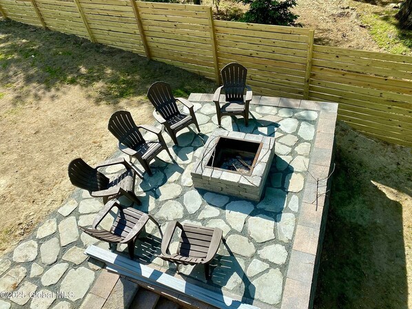 A patio with Adirondack chairs and a stone fire pit.