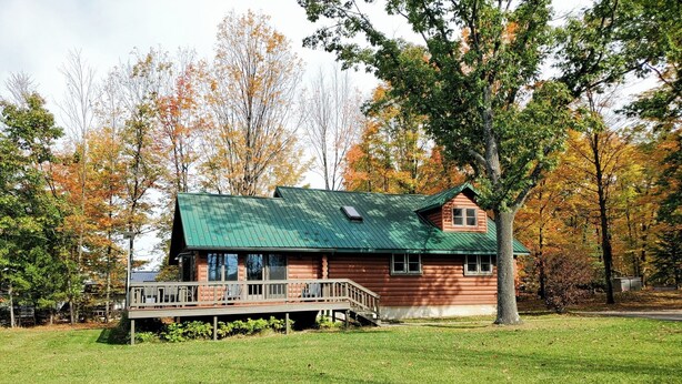 Une cabane en rondins avec un toit végétalisé, une terrasse et un foyer extérieur dans le jardin.