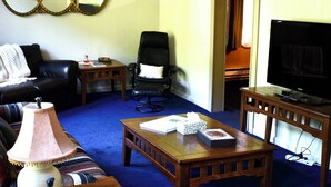 A living room with a blue carpet, a wooden coffee table, a sofa, a TV stand, and a chair. - Train View a spacious 3-bedroom upstairs apartment with WiFi in Northfork (Northfork)