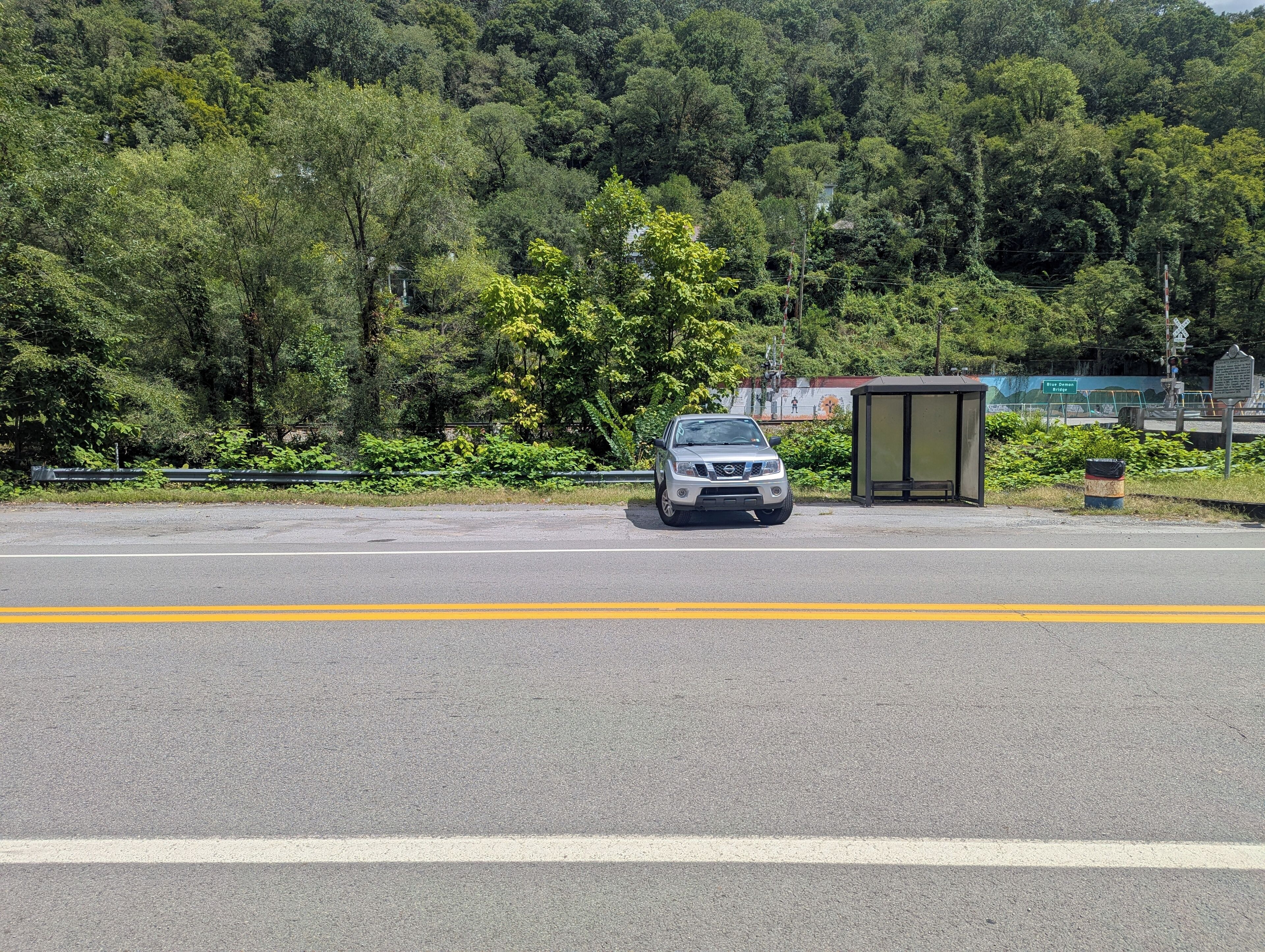 A road with a bus stop and a car parked on the side.