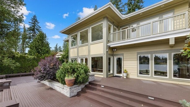 A two-story house with a deck, large windows, and a view of a lake.
