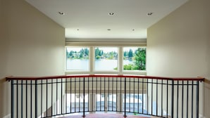 A spacious balcony with a wooden floor and a black metal railing, overlooking a lake and greenery.