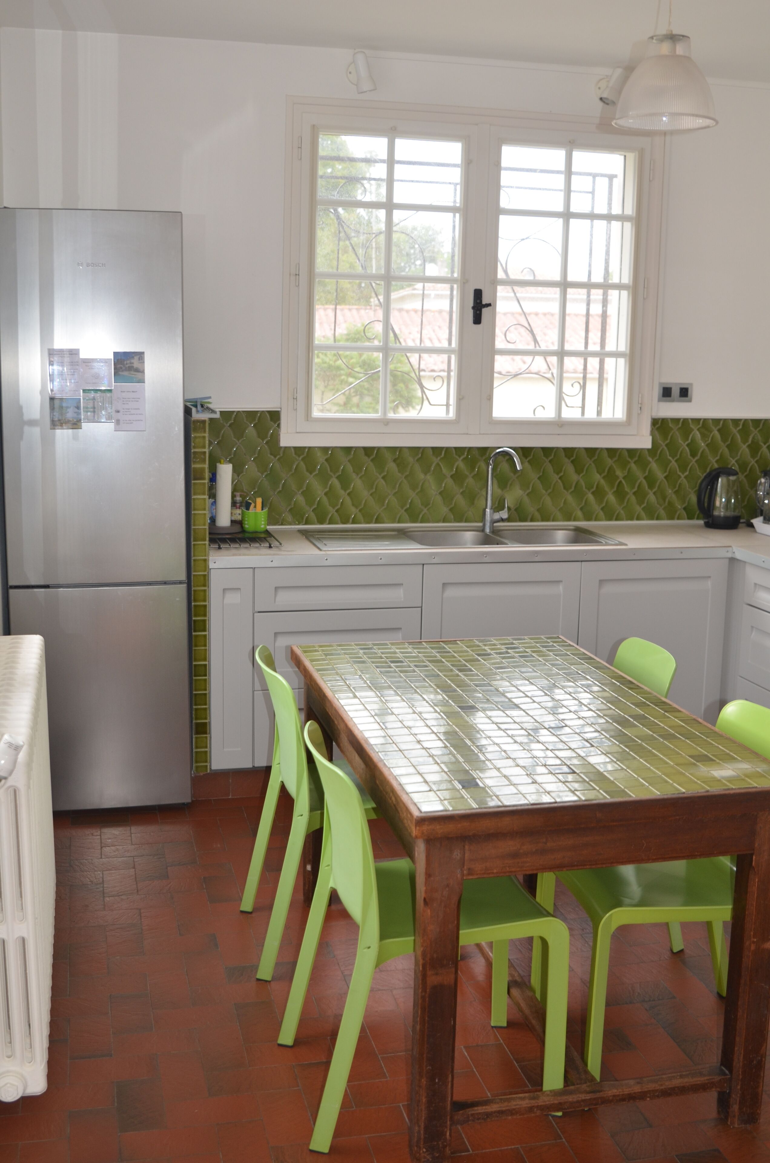 A kitchen with a stainless steel refrigerator, a window with a view, a sink, and a table with chairs.