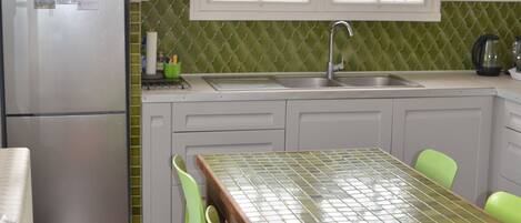 A kitchen with a stainless steel refrigerator, a window with a view, a sink, and a table with chairs.