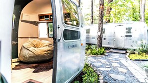 Interior de una camper con un sillón de gusa, una pequeña cocina y una zona de estar para dormir.