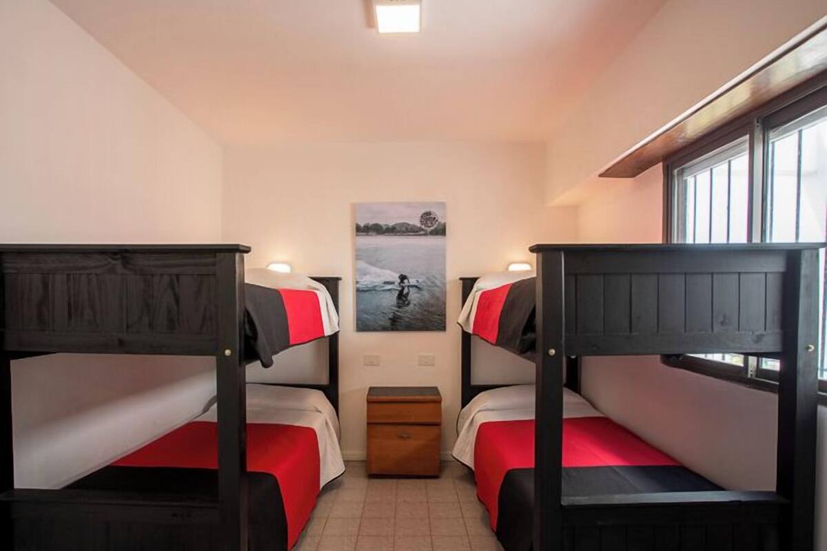 Um quarto com beliches, um pequeno baú de madeira e um quadro pendurado na parede.