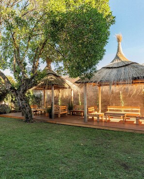 A garden with thatched-roof structures, wooden benches, and a large tree. - Las Golondrinas (Mar del Plata)