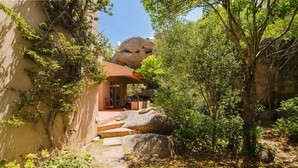 Un sendero conduce a un edificio de techo rojo, rodeado de rocas grandes y vegetación.