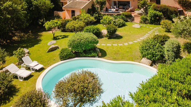 Una villa moderna con piscina, rodeada de exuberante vegetación y paisaje rocoso.