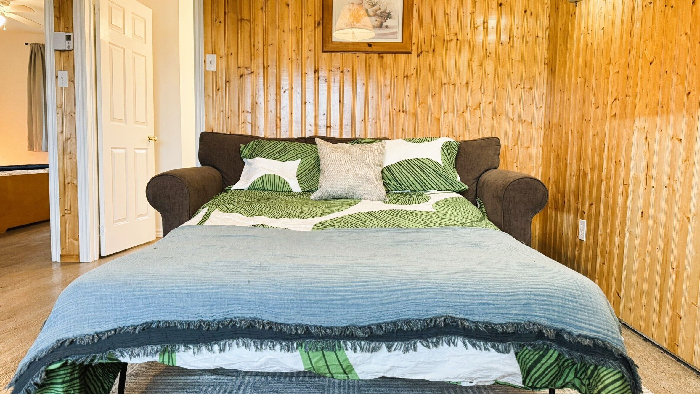 Ein Bett mit blauer Steppdecke und grün gestreiften Kissen in einem Zimmer mit holzgetäfelten Wänden.