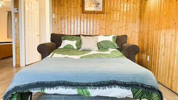Ein Bett mit blauer Steppdecke und grün gestreiften Kissen in einem Zimmer mit holzgetäfelten Wänden.